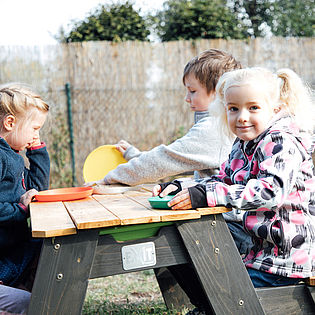 Kindergartenkinder sitzen am Tisch im Freien