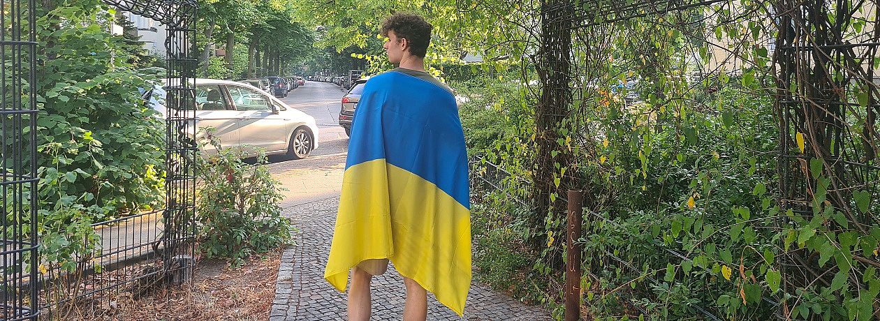 Ein junger Mann mit einer großen ukrainischer Flage auf dem Rücken
