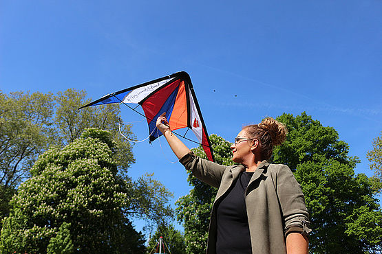 Eine Frau mit einem Flugdrachen mit dem Stephanus-Stiftung-Logo und dem Motto Aufwind-Pflege drauf