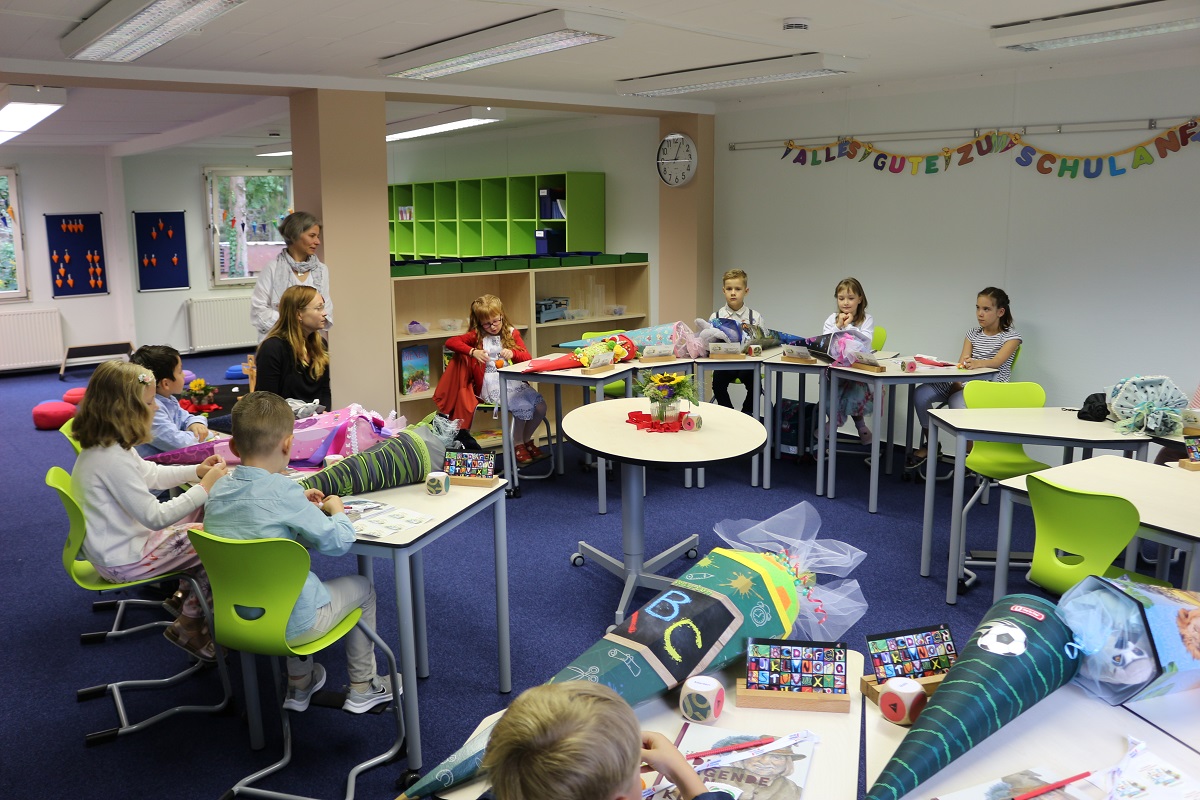 Einschulungskinder sitzen an den Tischen im Klassenraum  und werden von den Lehrer begrüßt