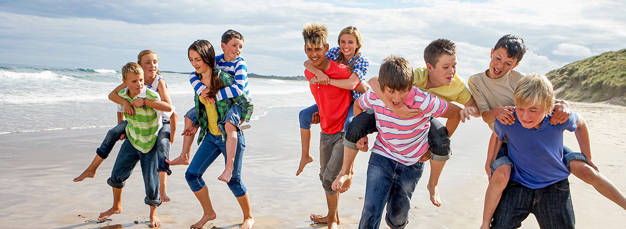 Kinder und Teenager spielen Huckepacktragen am Strand