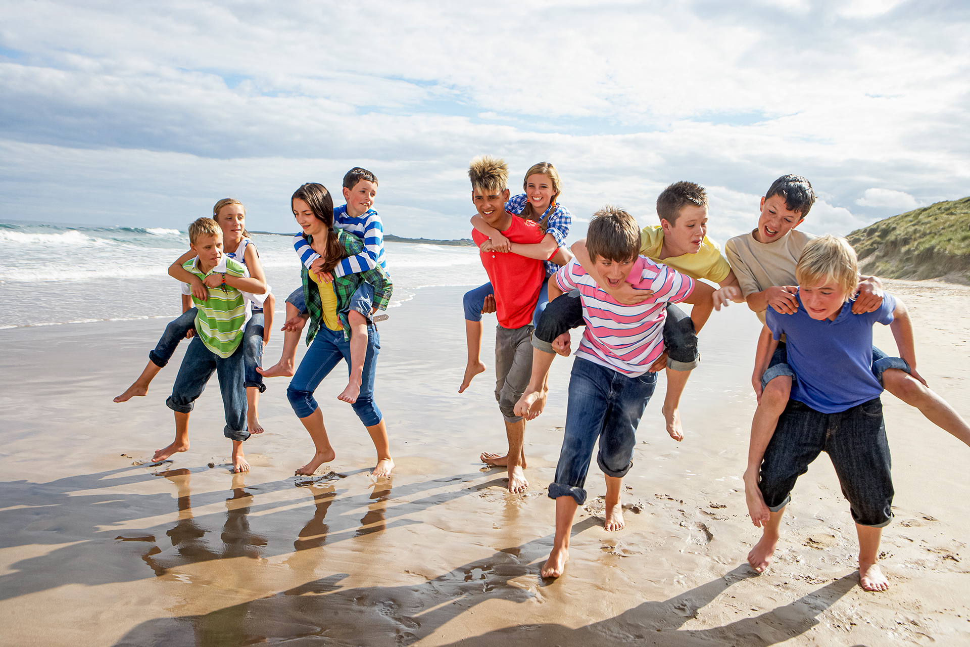 Kinder und Teenager spielen Huckepacktragen am Strand
