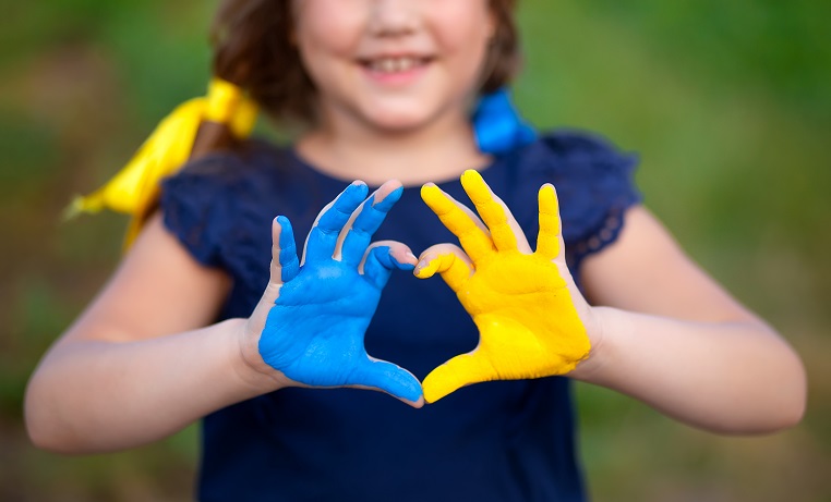 Hände eines Kindes im Form eines Herzes bemahlt mit Ukraineflage