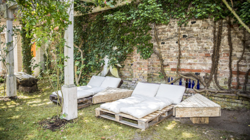 Mehrere Holzliegen mit weißen Matratzen stehen in einem grünen Garten