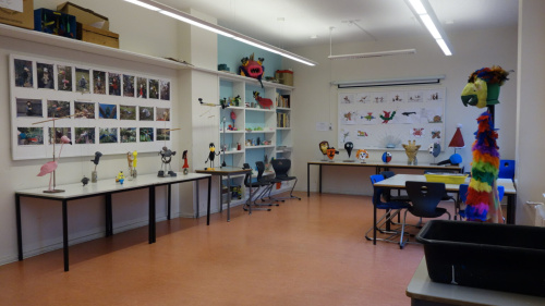 Zwei Whiteboards mit Fotos von Kunstwerken, sowie Tische und Regale mit Kunstwerken von Schülern.