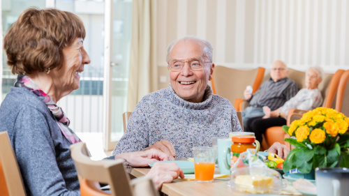 En älterer Herr sitzt mit anderen Seniorinnen am Frühstückstisch.