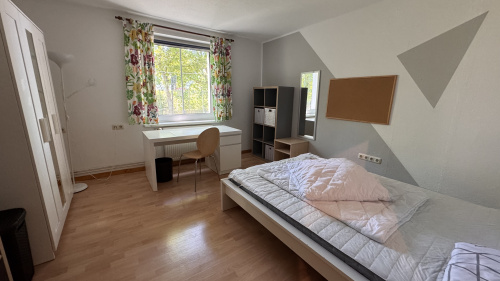 Ein Schlafzimmer mit Bett, Schrank und Schreibtisch am Fenster