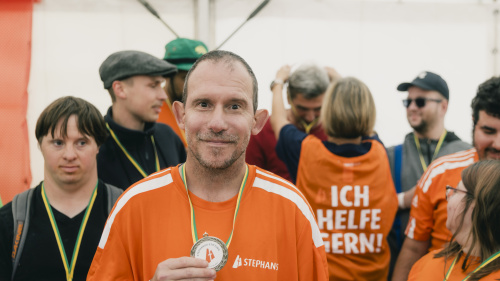 Mann in orangem Stephanus-Shirt zeigt stolz seine Medaille bei Sportveranstaltung