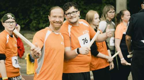 Zwei Männer im orangen Trikot halten Staffelstab bei Stephanus Lauf