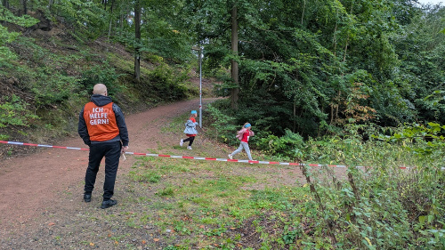 Zwei Läuferinnen laufen durch den Wald um eine Kurve. Links sieht man einen Streckenposten.