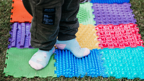 erson läuft in Socken über einen bunten Fühlpfad im Freien.