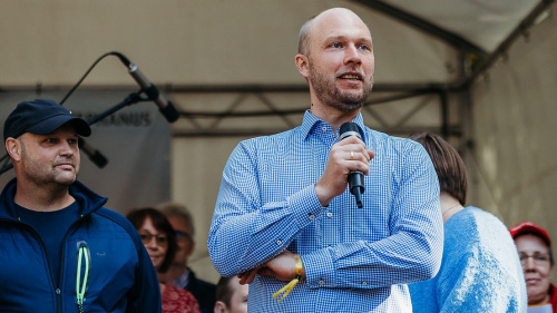 Person spricht mit Mikrofon auf einer Bühne vor Publikum.