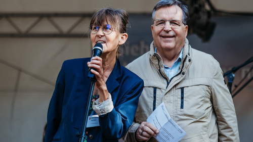 Zwei Personen auf Bühne, eine spricht ins Mikrofon, beide lächeln.