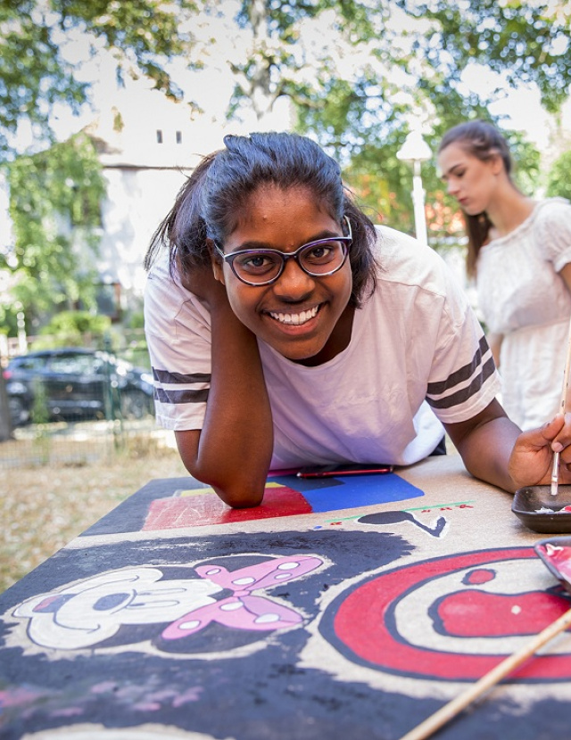 Junge Frau malt mit Pinsel ein Bild auf ein großes Plakat. 