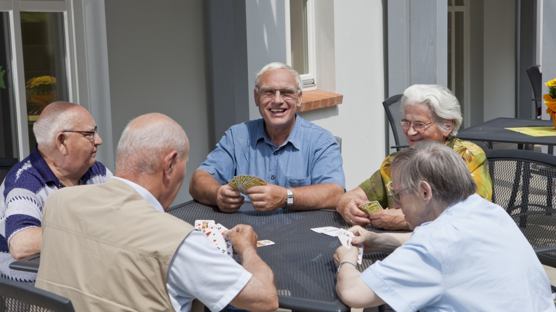 Fünf Senior*innen sitzen am Tisch und spielen ein Kartenspiel