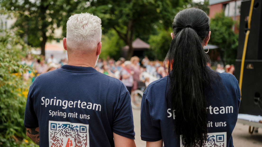 Ein Mann und eine Frau stehe mit den Rücken zur Kamera. Auf den T-Shirts steht Springerteam.