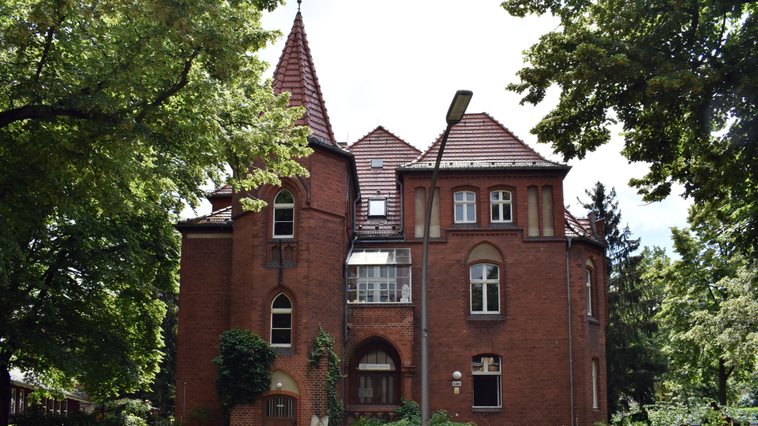 Ein altes Backsteingebäude mit einem Turm und großen Fenstern. Es wurde circa 1900 erbaut.