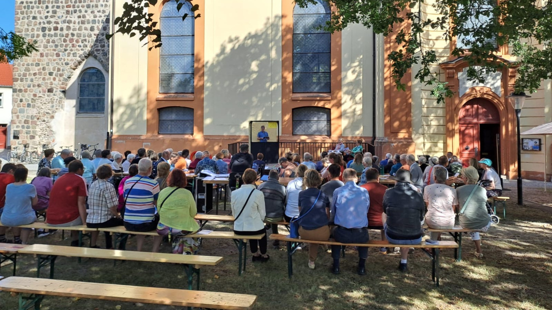 Menschen sitzen auf Bänken vor der Maria Magdalenenkirche in Templin