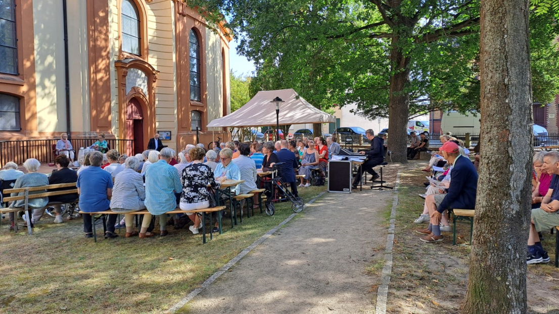 Menschen sitzen auf Bänken vor der Maria Magdalenenkirche in Templin