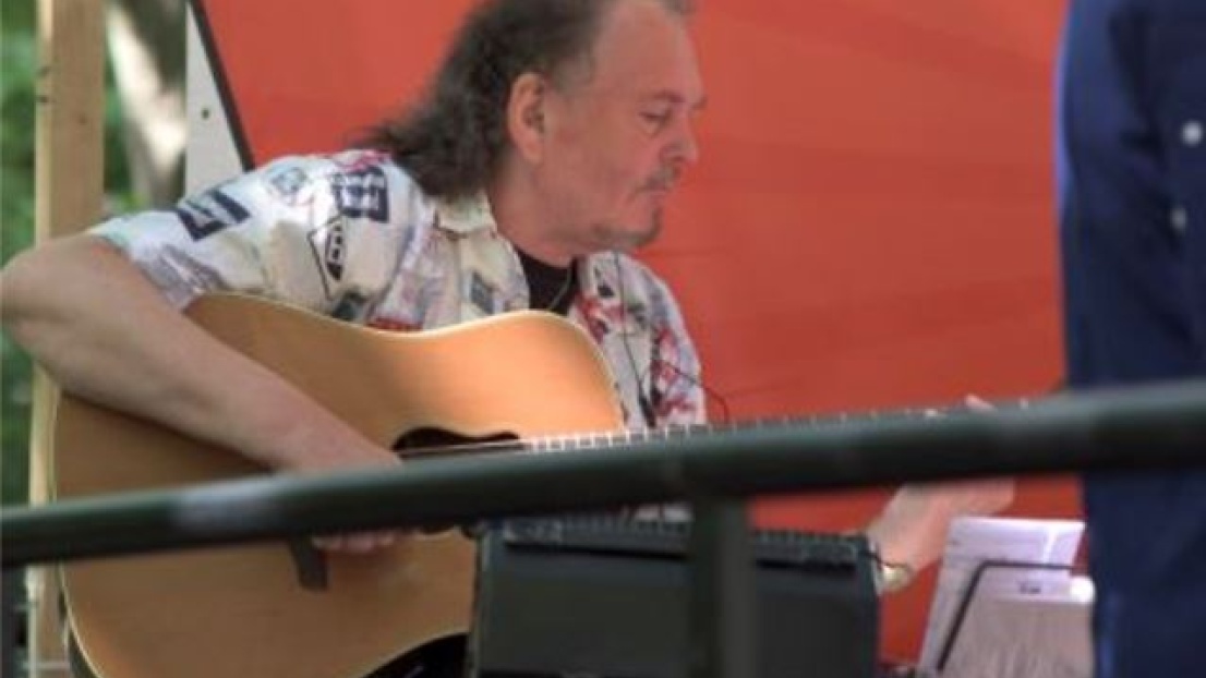 Auf einer kleinen Bühne im Freien sitzt ein Musiker und spielt konzentriert auf einer Gitarre.