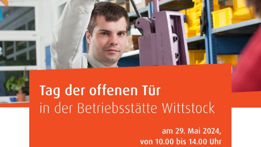 Ein junger Mann steht in einer Werkstatt und betätigt den Hebel einer Maschine. Er lächelt. Im Hintergrund befinden sich Lagerregale. 