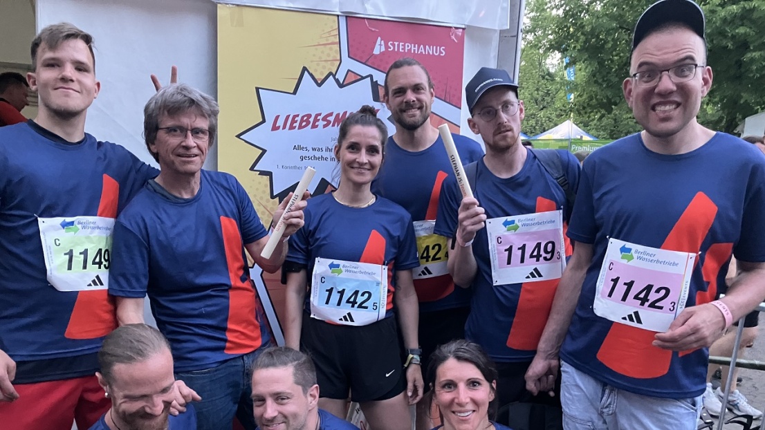 Eine Gruppe von fröhlich-motivierten Menschen schaut in die Kamera. Sie tragen alle das selbe Trikot mit dem Stephanus-Glockenstuhl-Logo und einer Laufnummer. Zwei halten einen Staffelstab in der Hand.