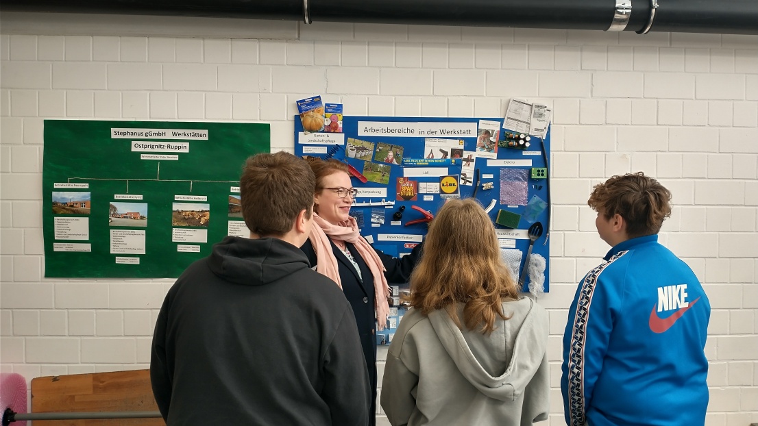 Schülerinnen und Schüler stehen vor einem Plakat und lassen sich in der Stephanus-Werkstatt die Arbeitsbereiche erklären.