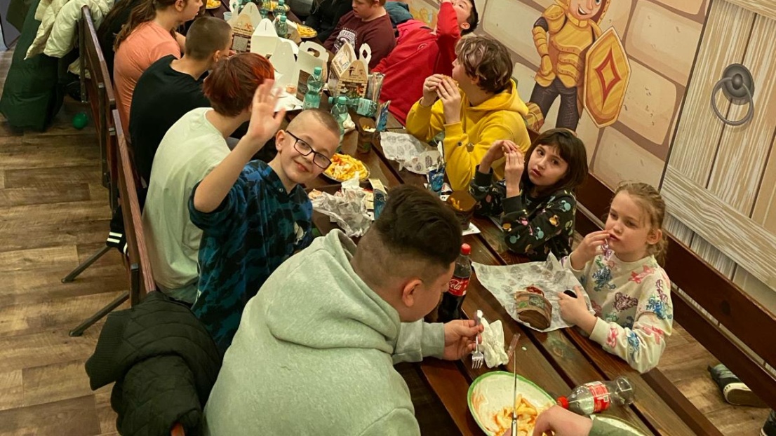 Kinder und Jugendliche essen zusammen an einer großen Tafel innerhalb des Spielelands