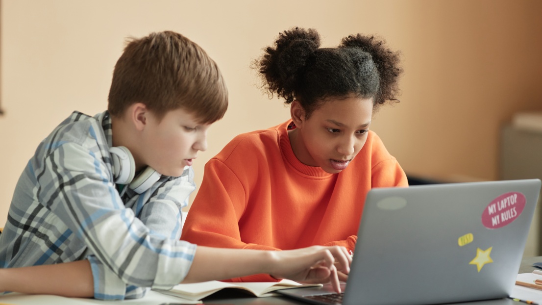 Ein Mädchen und ein Junge schauen gemeinsam auf den Bildschirm eines Laptops.