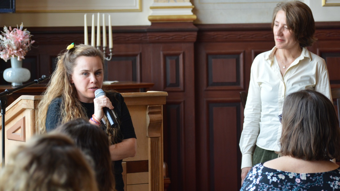Die Vorstandsvorsitzende der Stephanus-Stiftung, Dr. Ellen Ueberschär, und die Koordiantorin der Anlaufstelle für Alleinerziehende in Treptow-Köpenick, Dana Moser, stehen vor einem Publikum. Frau Moser spricht in ein Mikrofon.