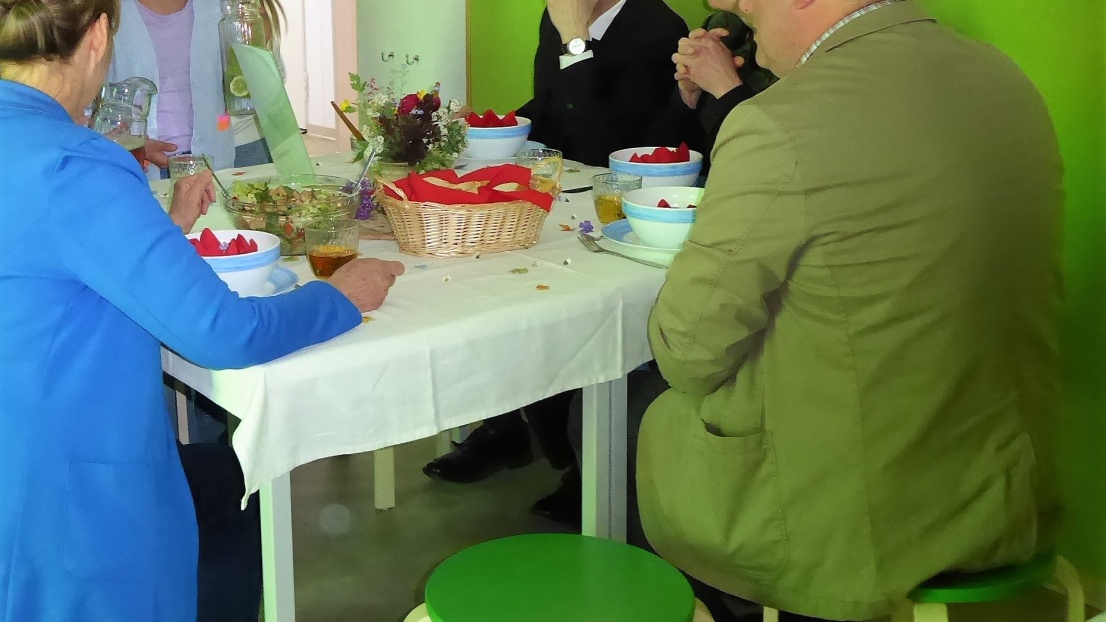 Erwachsene Menschen sitzen an einem bunt gedeckten Frühstückstisch und werden von Kindern bedient.