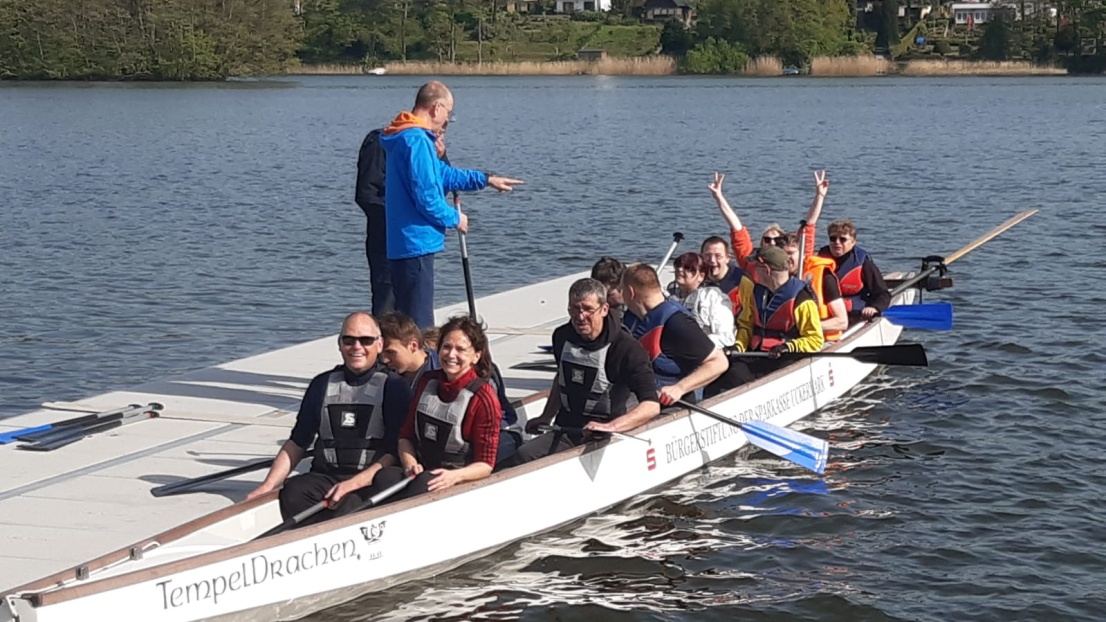 Menschen sitzen in einem Drachenboot und jubeln in die Kamera.