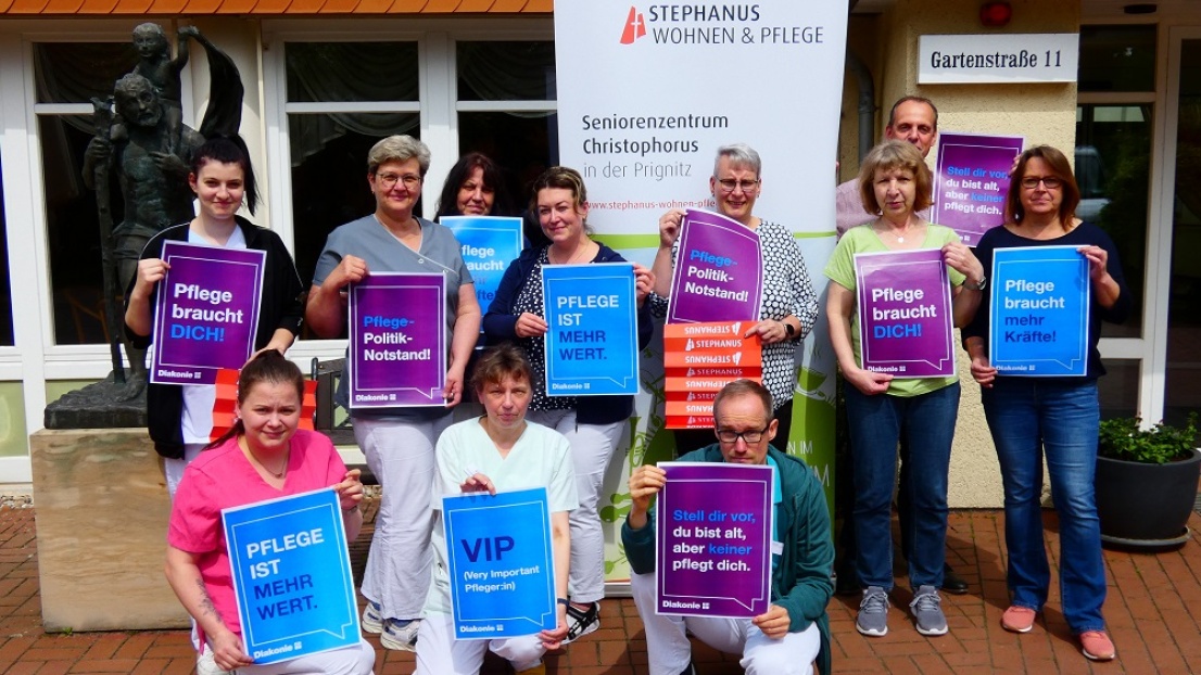 Mitarbeitende des Seniorenzentrums Christophorus lächeln in die Kamera und werben mit Bannern und Plakaten für den Pflegeberuf