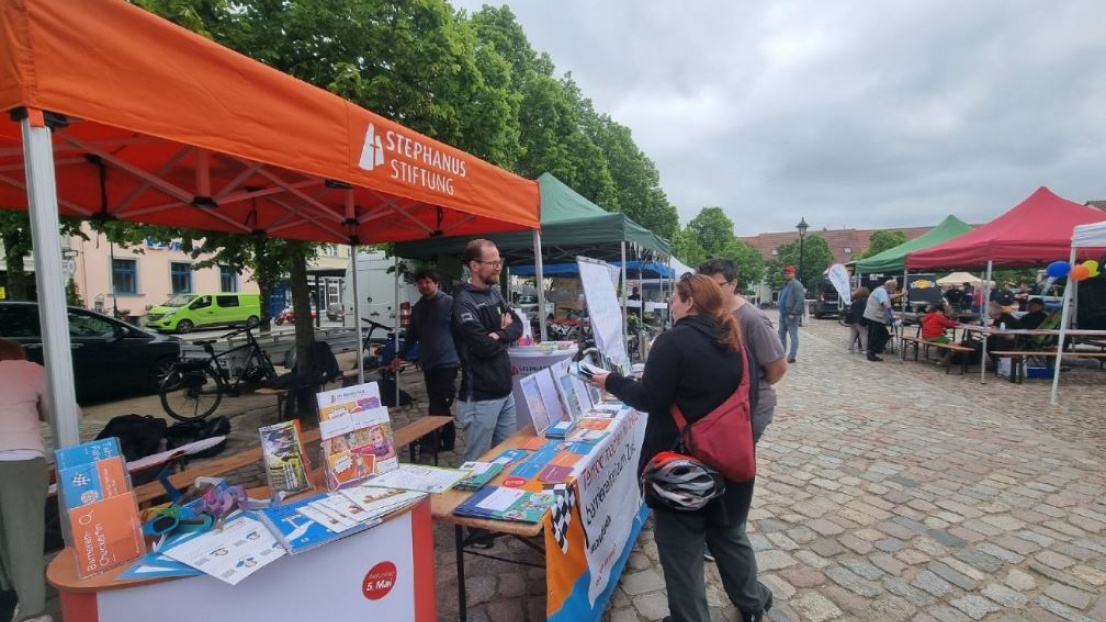 Passant*innen unterhalten sich an einem Aktoinsstand der Stephanus-Stiftung mit einem Mann, der dahinter steht und Flyer bereit hält