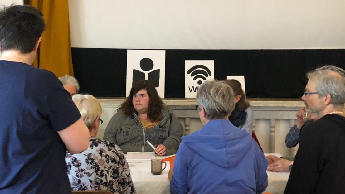 Mehrere Menschen sitzen konzentriert an einem Tisch und sprechen miteinander. Sie arbeiten an Textübersetzungen.