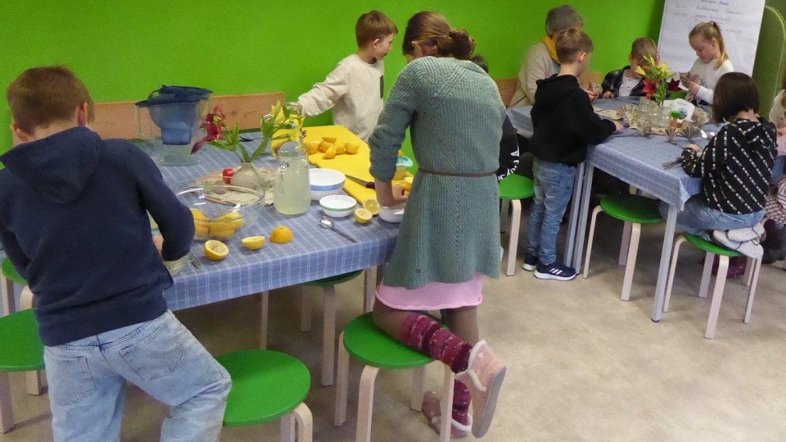 Kinder stehen an kleinen Tischen und bereiten Zitronenlimonade zu