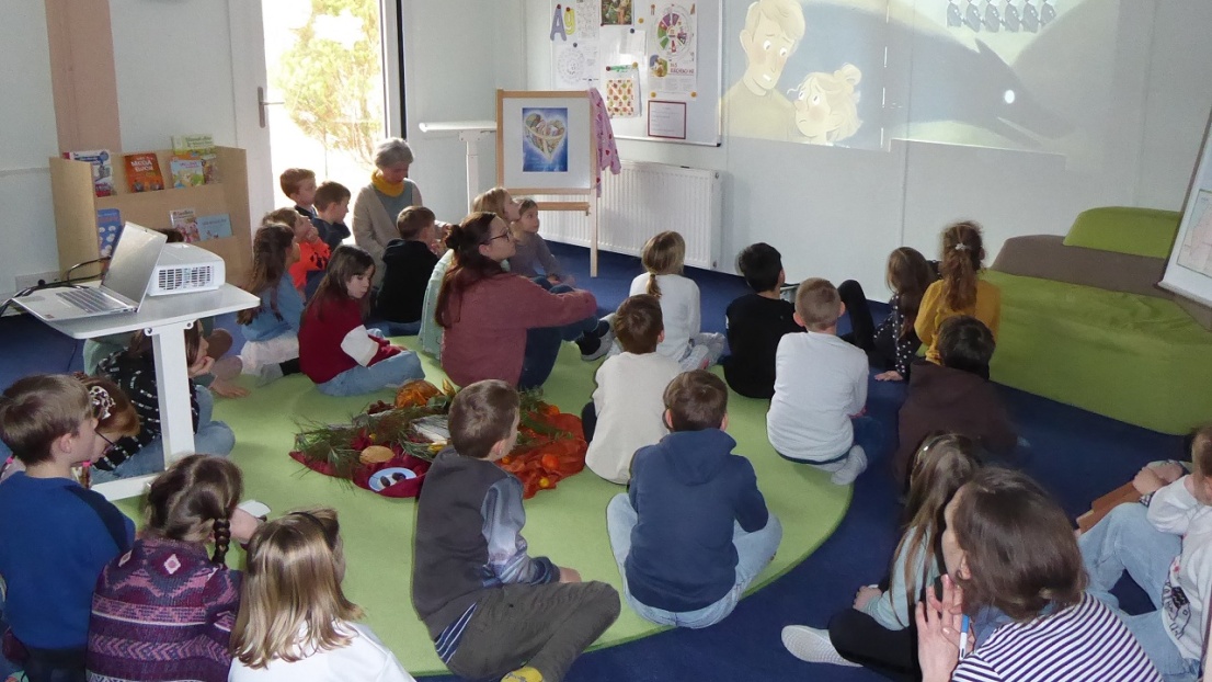 Viele Kinder sitzen in einem Raum auf dem Boden und schauen einen Animationsfilm, der an die Wand projiziert wird