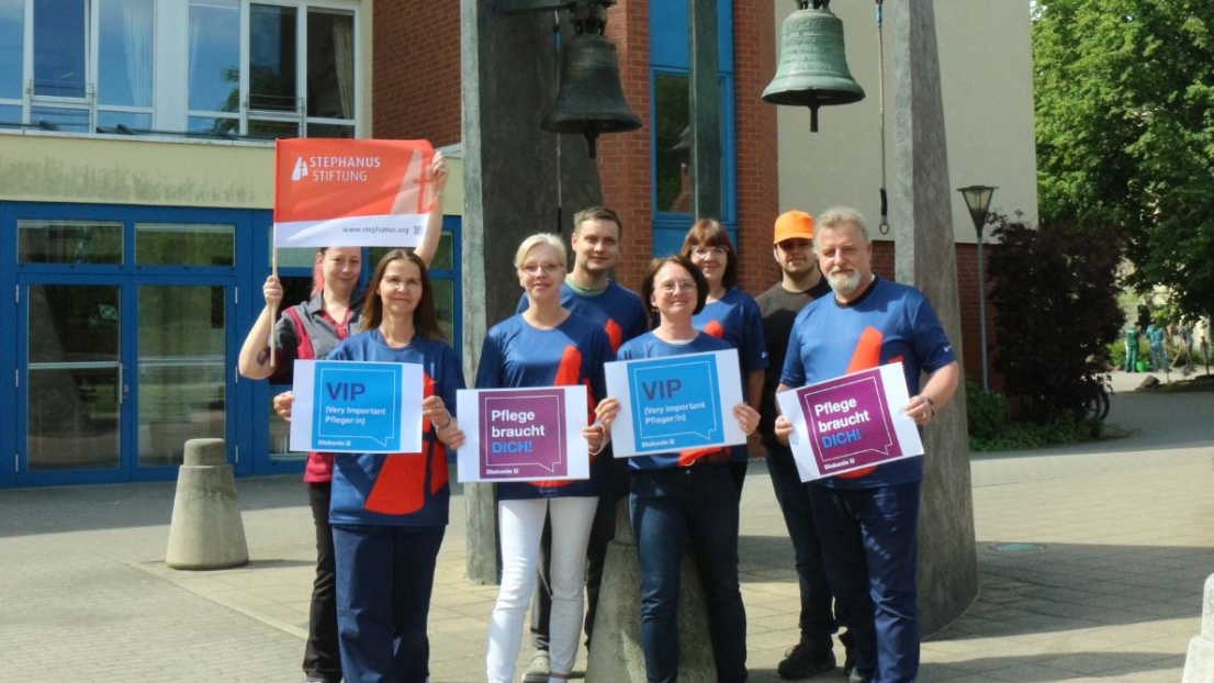 Mitarbeitende des Ernst-Berendt-Hauses in Berlin-Weißensee lächeln in die Kamera und werben mit Bannern und Plakaten für den Pflegeberuf
