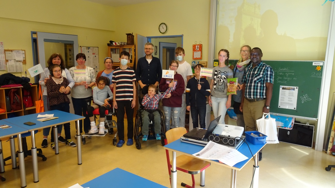 Gruppenfoto in einem Klassenraum mit Roland Mulondo und einigen Schülerinnen und Schülern und Lehrerinnen und Lehrern.