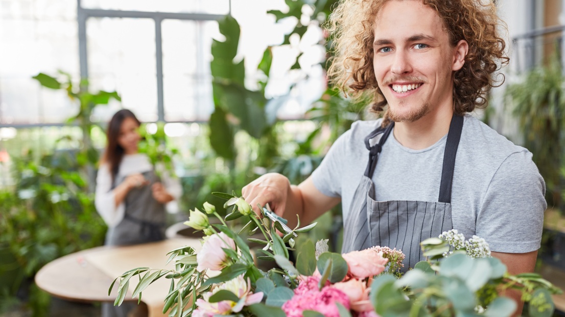 Junger Florist bindet einen bunten Blumenstrauß und lächelt in die Kamera.