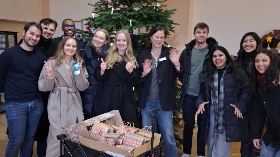 Viele junge Menschen stehen vor einem Weihnachtbaum und haben einen Bollerwaagen voll mit Geschenken