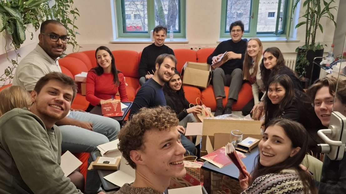 Viele junge Menschen sitzen zusammen und packen mit Freude viele Geschenke.