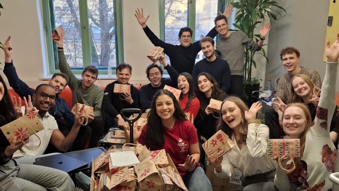 Viele junge Menschen sitzen zusammen und präsentieren mit Freude viele verpackte Geschenke.