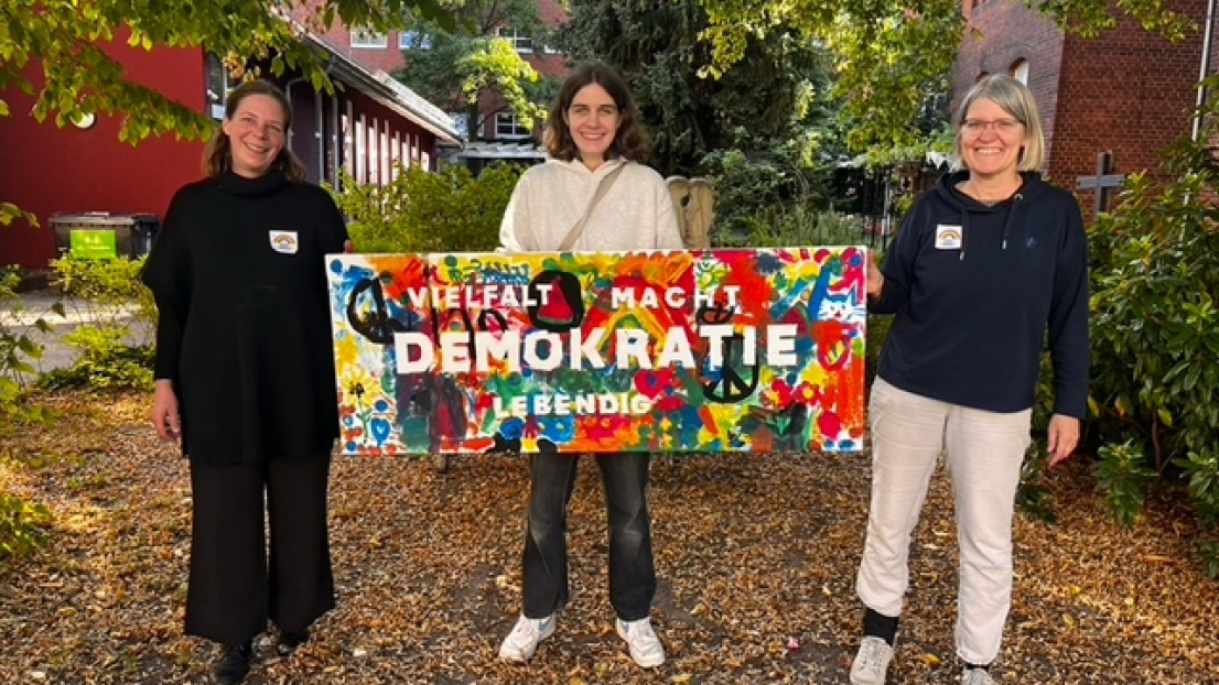 Drei Frauen stehen und halten zusammen ein selbstgemachtes Schild mit Schriftzug Demokratie