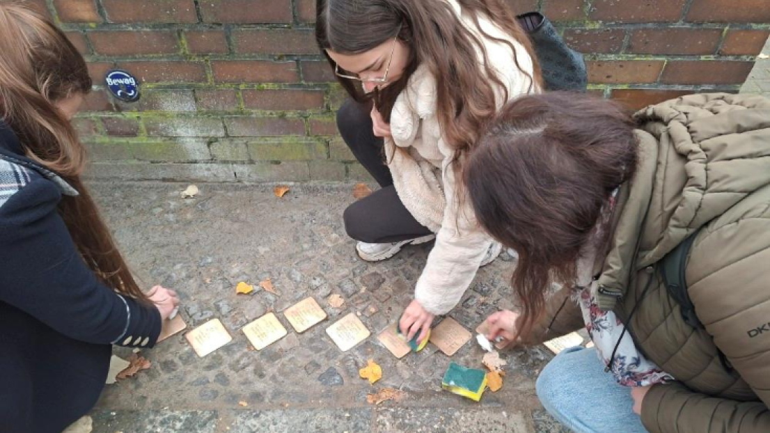 Drei junge Mädchen machen die Stolpersteine auf dem Pflasterweg sauber.