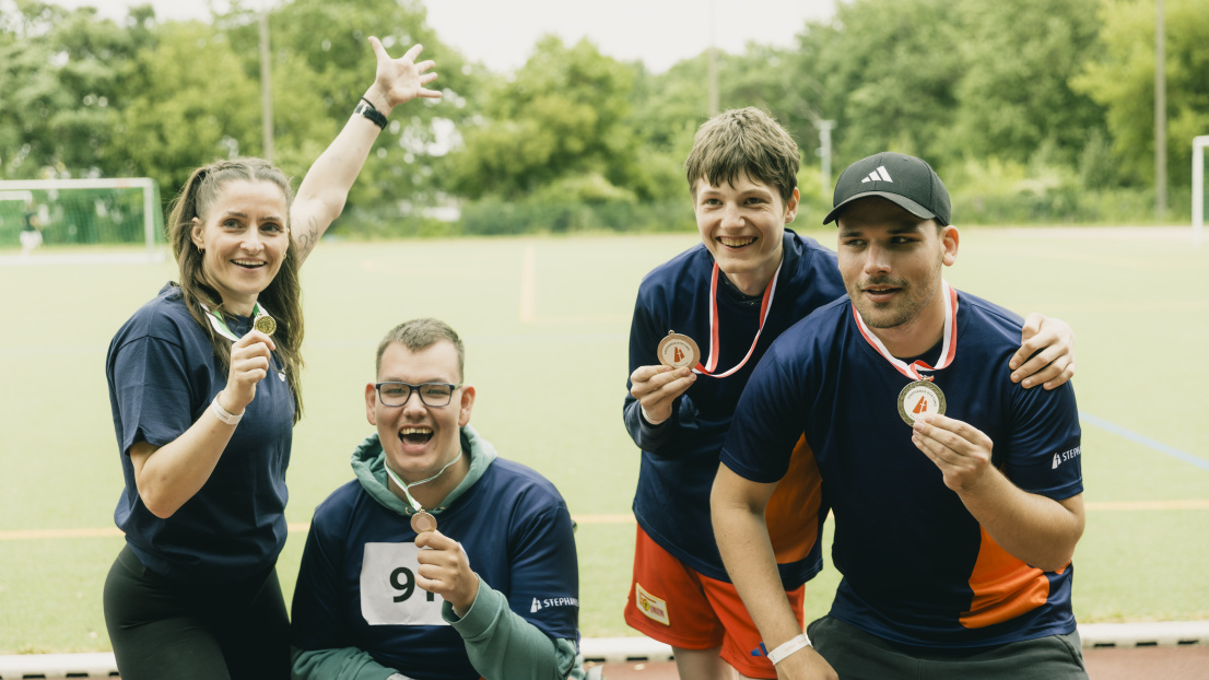 Vier Sportler zeigen stolz ihre Medaillen, einer sitzt im Rollstuhl