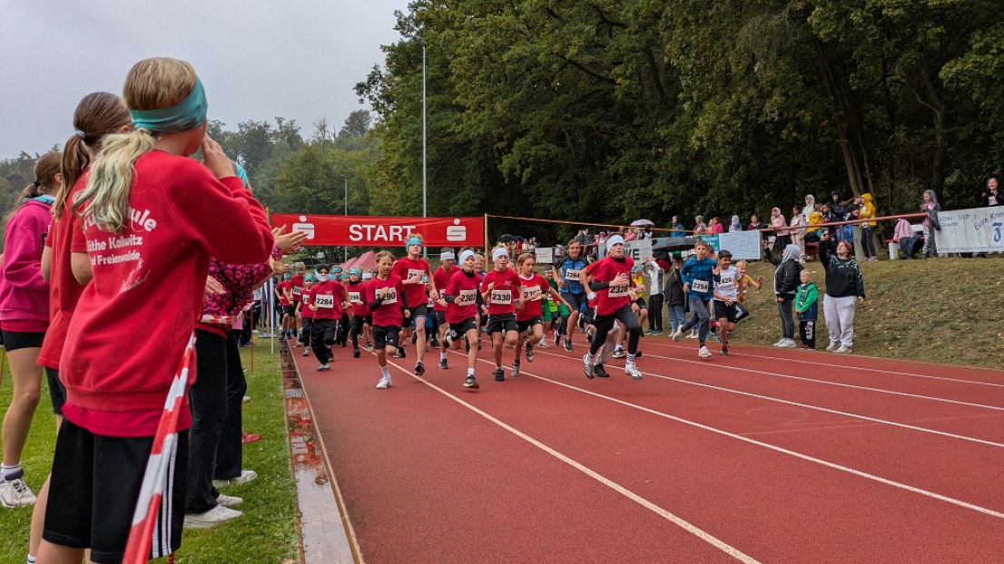 Viele Schülerinnern und Schüler starten bei einem Lauf. Sie rennen, im Hintergrund hängt das Start-Banner.