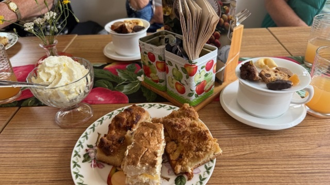 Auf dem Tisch stehen drei Stück Kuchen, Sahne, zwei Teetassen und ein Teller mit Keksen.