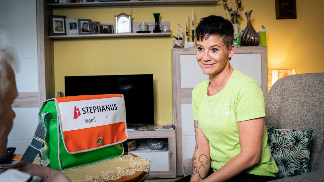Eine lächelnde Pflegekraft von Stephanus Mobil sitzt einer Seniorin gegenüber