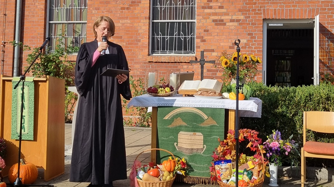 Pastorin steht am Altar vor der Kirche, der mit Obst und Gemüse aus der Ernte geschmückt ist.